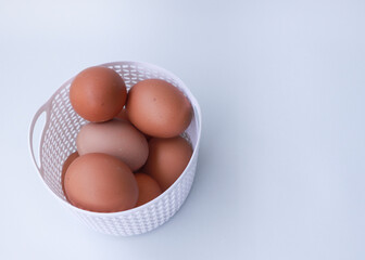 Raw chicken eggs in white basket on white background