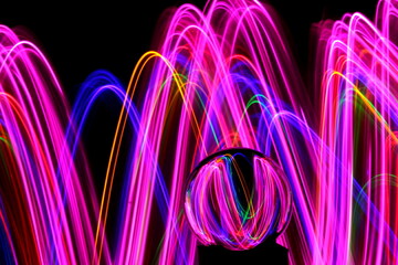 Long exposure photograph of neon multi colour in an abstract swirl, parallel lines pattern against a black background with reflections in a glass crystal ball. Light painting photography.