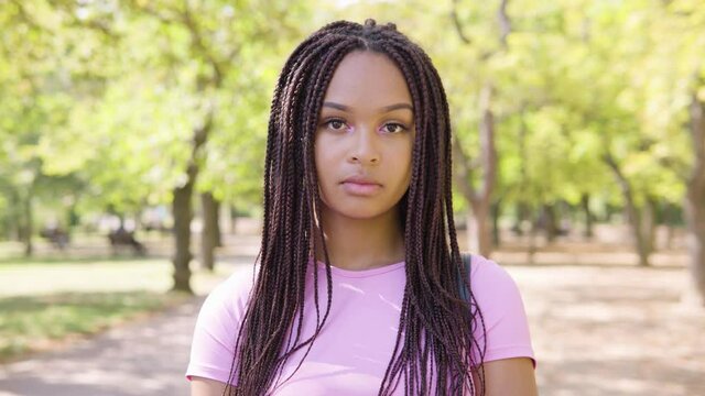 A young black woman looks seriously at the camera in a park on a sunny day - closeup