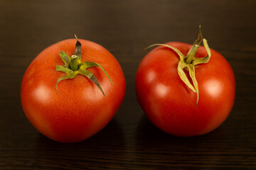 A red tomato with a green tail lies in the hand against a dark textured wooden background. Eco-friendly tomatoes. Fresh tomatoes. Tomatoes with water drops. Fresh vegetables