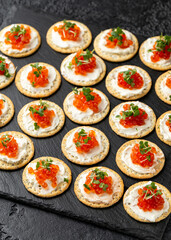 Salmon caviar and soft cheese savory crackers with sesame and poppy seeds served on black slate board