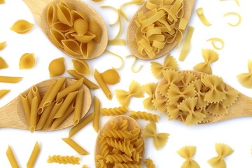 Five types of pasta lie on wooden spoons on a white background