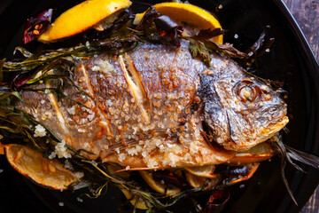 Fried dorado fish with lemon and sea salt close-up on a black background.