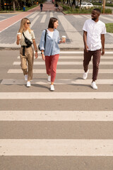 Obraz premium Two girls with drinks talking to African guy in casualwear while crossing road