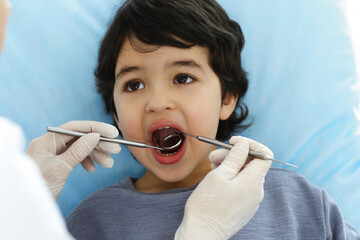 Cute arab boy sitting at dental chair with open mouth during oral checking up with doctor. Visiting dentist office. Stomatology concept