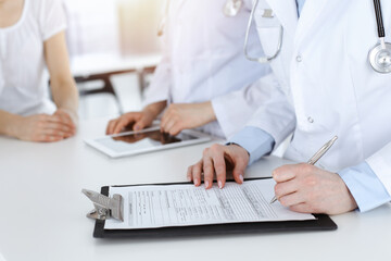 Fototapeta premium Unknown woman-doctors at work consulting patient. Female physicians filling up medical documents or prescription, close-up