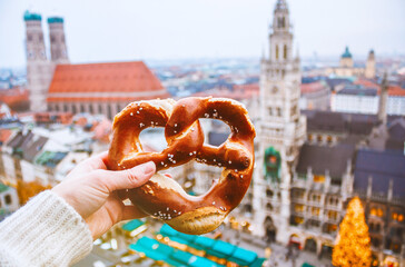 Hand with bretzel against the background of the panorama of Munich and the Christmas fair. Munich,...