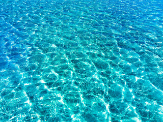 Transparent turquoise-blue sea water against the background of white sand at the bottom, top view....