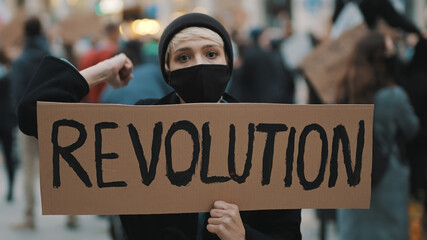 Revoultion concept. Young woman with face mask and banner protesing in the crowd. High quality photo