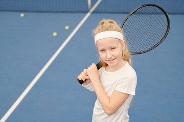 Adorable little girl in activewear holding tennis racket during play on stadium