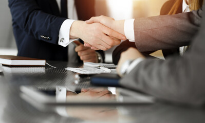 Unknown businessman shaking hands with his colleague or partner above the desk in sunny office, close-up