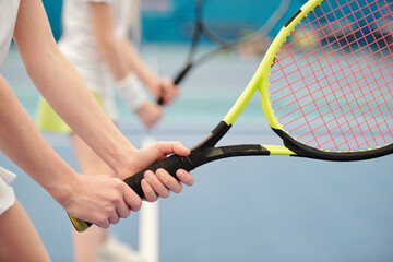 Hands of active girl standing on stadium against field and holding tennis racket