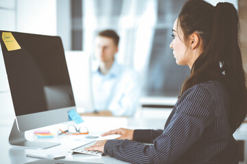 Business woman using computer at workplace in modern office. Brunette secretary or female lawyer smiling and looks happy. Working for pleasure and success