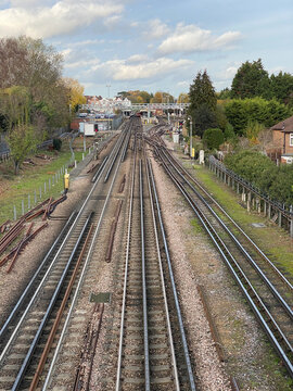 Underground railway tracks in the countryside surrounded by trees with a train station in the distance.