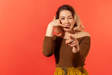 Portrait of young pretty woman with blonde hair smiling, showing a gesture of a phone and ask you...