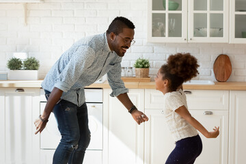 Funny cooking with dad. Happy laughing millennial black father dancing disco at modern designed kitchen with overjoyed little kid daughter jumping listening to music enjoying active leisure having fun