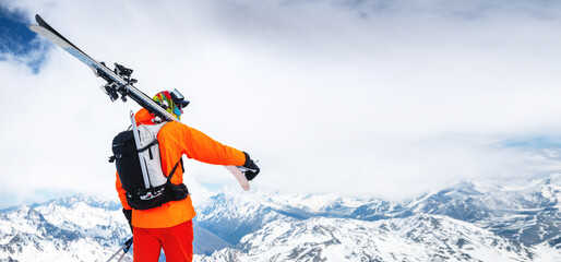 Panoramic portrait of a stern climber skier in sunglasses and a cap with a ski mask on his face. holds his skis on his shoulder and looks away against of Mount Elbrus