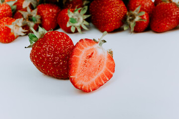 Fresh strawberries on a white background. Two sliced strawberries on the background of a hill of strawberries. Group of ripe strawberries with green leaves close-up. Ingredients for juice.