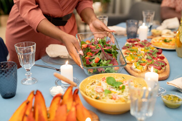 Hands of African woman putting glass bowl with fresh vegetable salad on table