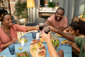 Happy young African female, her husband, teenage son and daughter toasting