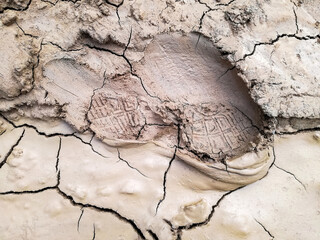 Boot footprint on the dried clay surface. Cracked dry soil with shoeprint. Shoe marks on clay soil. An imprint of the foot of man in shoe. Top view. Close-up. Selective focus.