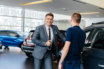 A young businessman with a salesman looks at a new car in a car dealership. Buying a car