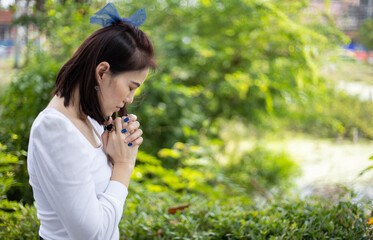 A woman in a white dress praying in the garden under the sunlight.