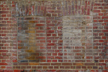 Old rough dirty brick wall facade with vintage detail of rectangular windows frame filled with brick.