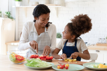 Cooking lesson. Happy patient black foster mom teaching little adopted daughter prepare healthy...
