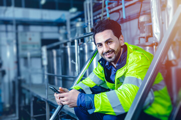 Portrait smiling happy smart latin engineer worker sitting relax in plant industry factory hand holding smartphone blue colortone effect.