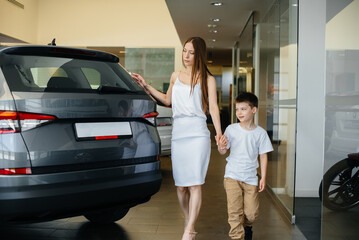 A happy mother with her young son chooses a new car at a car dealership. Buying a car