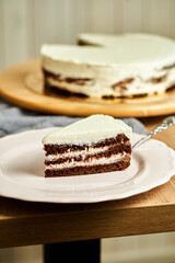Slice of three chocolate cake on plate. Board with delicious tasty homemade cake on table. Wooden background.