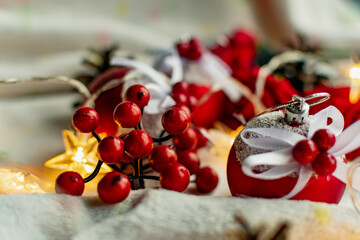 Christmas decorations on a soft cozy white blanket. Red toys in the form of balls and berries, with fir cones. Around yellow lanterns light bulbs in the form of stars. Elegant composition for Christma