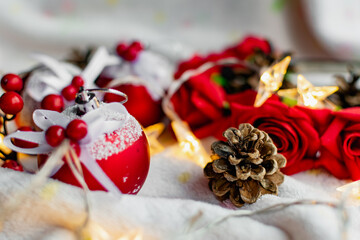 Christmas decorations on a soft cozy white blanket. Red toys in the form of balls and berries, with fir cones. Around yellow lanterns light bulbs in the form of stars. Elegant composition for Christma