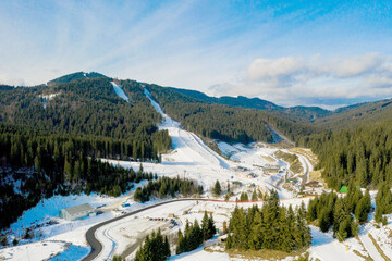 Aerial view of landscape of ski and snowboard slopes through pine trees going down to winter resort in Carpathians