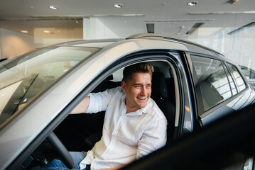 Fototapeta premium A happy young couple chooses and buys a new car at a car dealership. Buying a new car