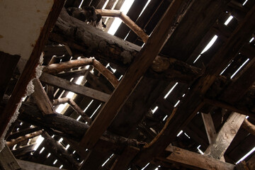 an attic made of wooden planks and beams with cracks from which sunlight comes out, destroyed...