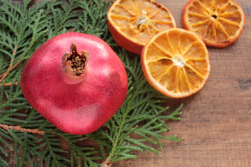 Obraz na płótnie Canvas Christmas background with fruits and Christmas tree branches. Pomegranate, dried orange slices and green twigs on wooden table. Flat lay winter holiday composition. Copy space