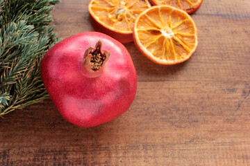 Christmas background with fruits and Christmas tree branches. Pomegranate, dried orange slices and green twigs on wooden table. Flat lay winter holiday composition. Copy space