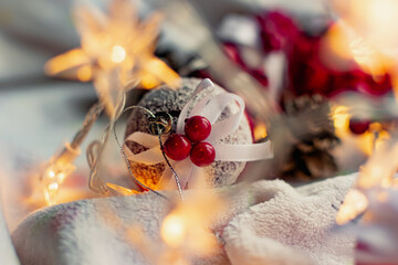 Christmas decorations on a soft cozy white blanket. Red toys in the form of balls and berries, with fir cones. Around yellow lanterns light bulbs in the form of stars. Elegant composition for Christma