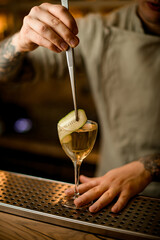 barman decorates cocktail glass with green cucumber slice using tweezers