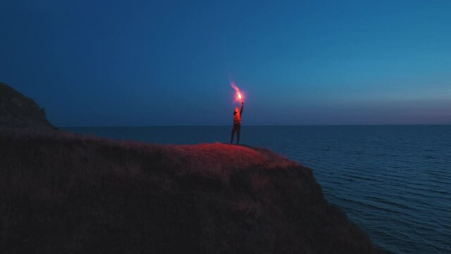 The man with a fire stick stands on the mountain cliff near the sea. slow motion