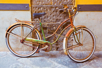 Fototapeta na wymiar Old rusty women's bicycle against a plaster wall in a italian street paved of stone