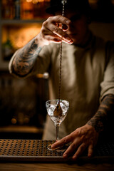 man bartender with long bar spoon stir the ice cubes in wine glass