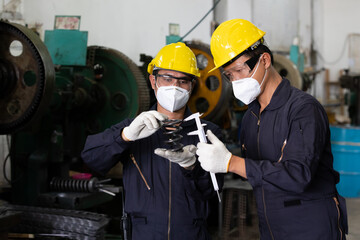 male couple technician or factory worker wearing face mask for protect virus, looking spring and measures a metal in factory