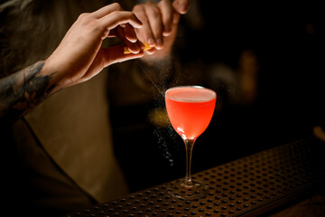 view of glass with cocktail on which man bartender sprays by lemon zest