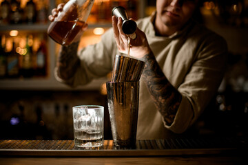 view of barman gently pours drink from metal jigger into shaker on bar counter