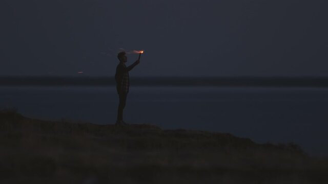 The man standing near the sea and holding a fire stick. slow motion