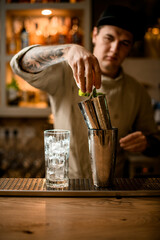 man bartender with his hand pours green leaves into steel shaker cup