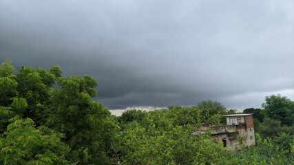 Fototapeta na wymiar Raining dark cloud over field in big farmland. dramatic rain clouds above the green field and buildings in India